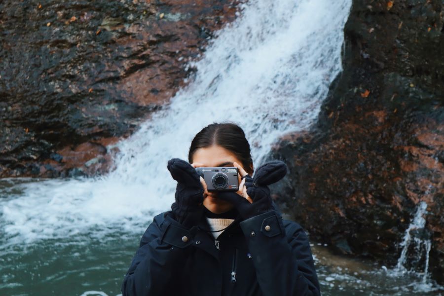 Woman taking photo with film camera in front of waterfall.