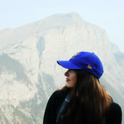 person in a blue cap standing for a profile portrait photograph in front of a hazy afternoon Mount Rundle along the ascent of Ha Ling Peak trail