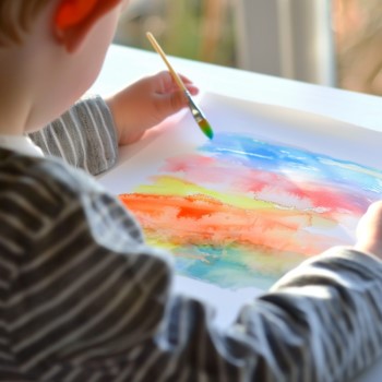 photo of a child painting a sunset or sunrise on a white piece of paper using watered down tempra paint